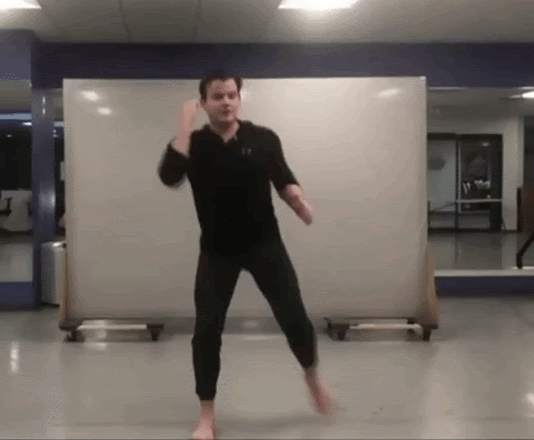 A gif of a man performing an exercise move. He is bringing his elbow to his knee while standing.