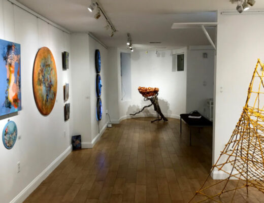 A gallery hallway featuring mixed media paintings and sculptures.